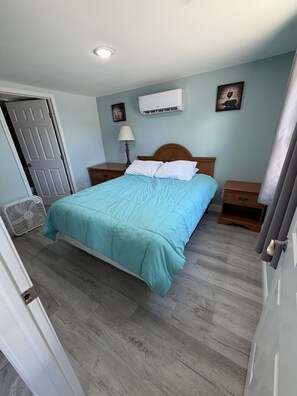 A bedroom with a bed, a nightstand, a lamp, an air conditioner, and a fan.