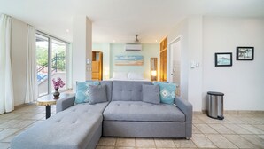 A modern living room with a grey sectional sofa, a small wooden side table with a vase, and a trash can. - Villa Elysian Beachfront Luna Studio Sleeps 4 (Provincia de Guanacaste)