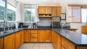 A modern kitchen with wooden cabinets, a black countertop, and a microwave. - Villa Elysian Beachfront Luna Studio Sleeps 4 (Provincia de Guanacaste)