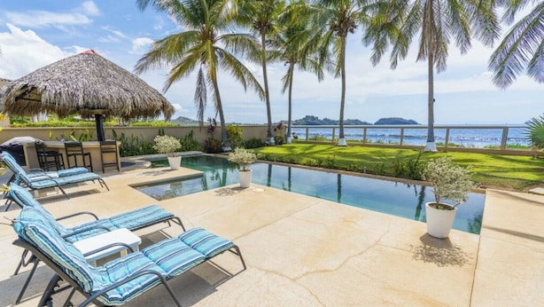 A pool area with lounge chairs, a thatched umbrella, and palm trees. - Villa Elysian Beachfront Luna Studio Sleeps 4 (Provincia de Guanacaste)