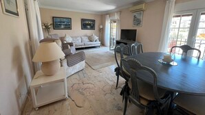 A living room with a sofa, a dining table with chairs, a TV, and artwork on the walls.