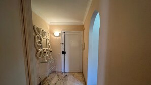 A hallway with a marble floor, a white door, and a wall-mounted light fixture.