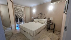 A bedroom with a large bed, a nightstand, a lamp, a ceiling fan, and a window with curtains.