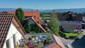 A residential area with red-tiled roofs, a balcony with a table and chairs, and a view of mountains in the distance. - Apartment "Haus Kaulitzki" with Lake View, Private Terrace & Wi-Fi (Wasserburg (Bodensee))