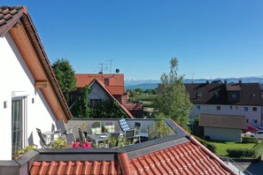 Una terraza en la azotea con mesa y sillas, vistas a casas vecinas y un cielo despejado.