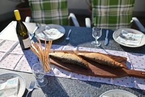 Una mesa de comedor con una botella de vino, un plato de pescado y una tabla de madera con pescado.