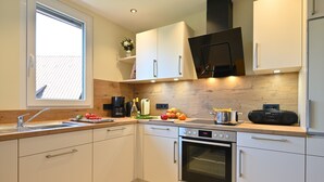 A modern kitchen with white cabinets, a built-in oven, a coffee maker, and a window. - Apartment "Haus Kaulitzki" with Lake View, Private Terrace & Wi-Fi (Wasserburg (Bodensee))