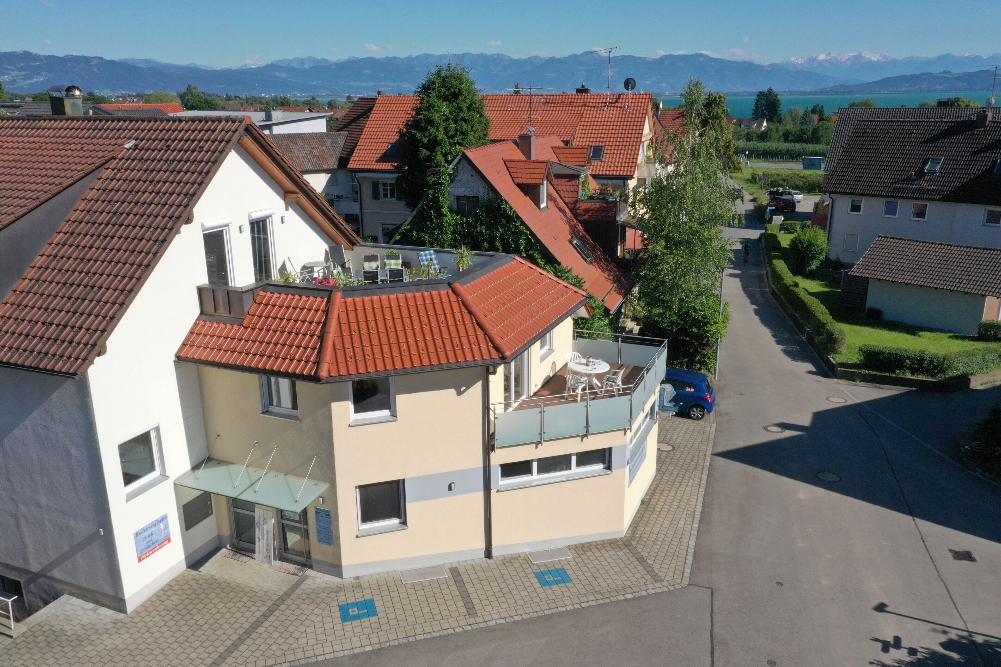 Um edifício residencial com telhado de telhas vermelhas, varanda com mobiliário exterior e vista desobstruída para montanhas ao fundo.