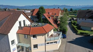 A residential building with a red-tiled roof, a balcony with outdoor furniture, and a clear view of mountains in the background. - Apartment "Haus Kaulitzki" with Lake View, Private Terrace & Wi-Fi (Wasserburg (Bodensee))