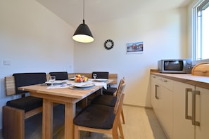 Zona pranzo con tavolo in legno, sedie nere, lampada a sospensione nera, orologio e forno a microonde sul piano di lavoro.