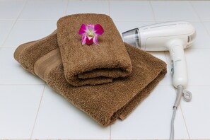 A folded brown towel with a pink orchid on top, and a white hair dryer beside it. - Haleakala (Naha)