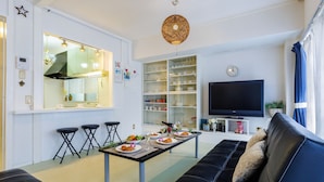 Un salón moderno con un sofá de cuero negro, una mesa de comedor con platos y vasos, una zona de cocina con un amplio ventanal y un televisor de pantalla plana.