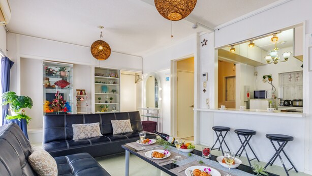 Una sala de estar moderna con un sofá negro, una mesa de centro de vidrio y un comedor con una mesa blanca dispuesta para una comida.