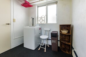 A compact room with a white refrigerator, a white stool, a wooden shelf with a basket, and a window with a metal gate. - Haleakala (Naha)