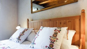 Een slaapkamer met een houten hoofdbord, twee decoratieve kussens, een bedlampje en een spiegel aan de muur.