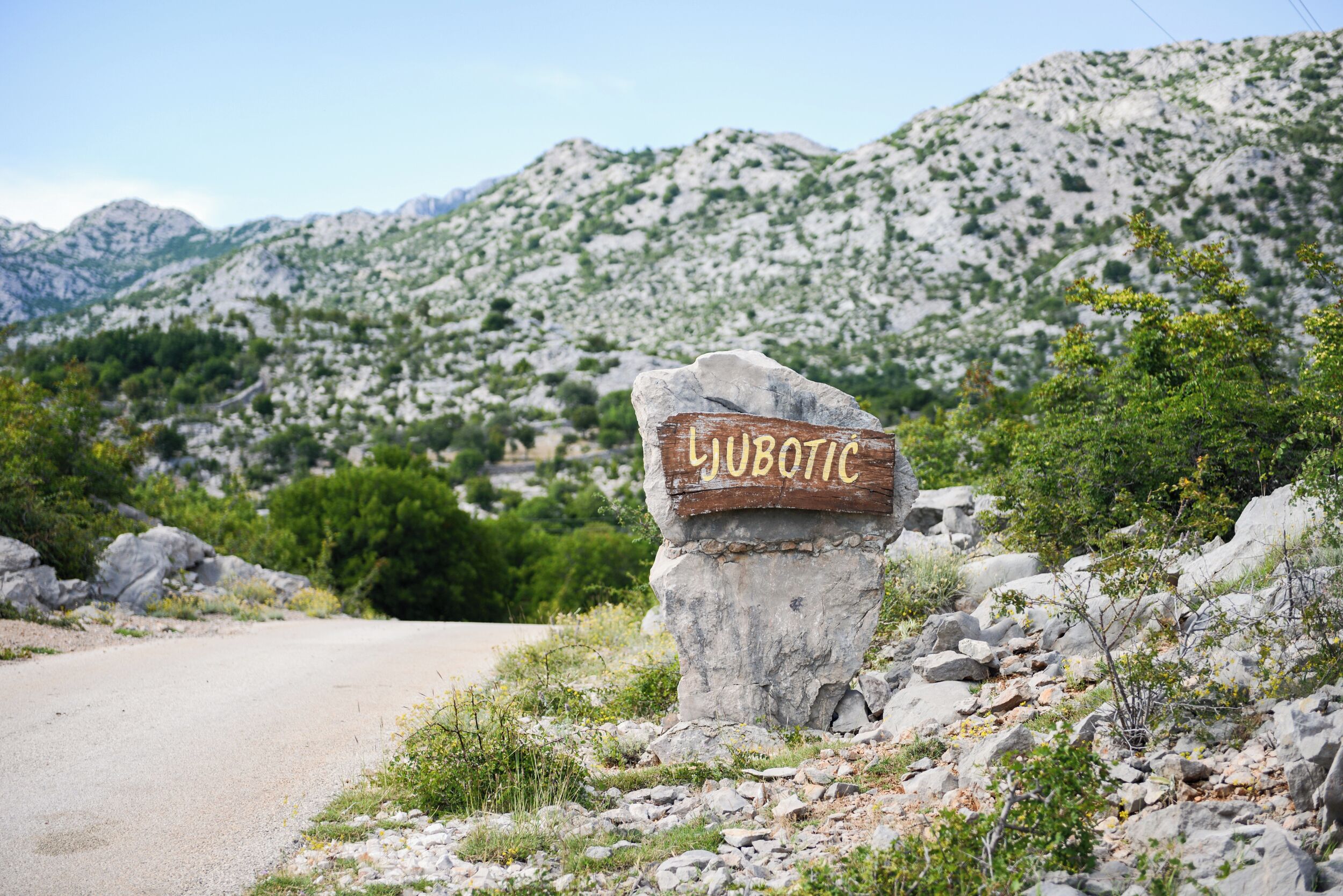 Un senyal de carretera amb el nom 'LUBOTIC' en un entorn rural, amb muntanyes al fons.