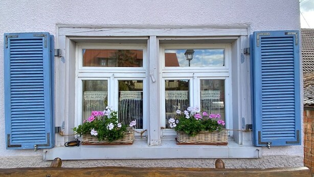 A building with white window frames and blue shutters, featuring two windows with wicker baskets containing flowers. - Holiday Home 'Altes Rathaus' with Terrace & Wi-Fi (Leibertingen)