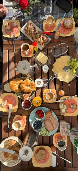 Ein Holztisch mit einer Auswahl an Frühstücksartikeln, darunter Croissants, Käse, Brot, Eier und Früchte.