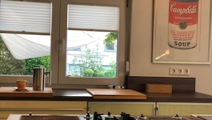 Una cocina con estufa a gas, cafetera y ventana con persianas.
