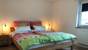 Una cama con colcha a cuadros, dos lámparas de noche, un mesita de noche de madera y una ventana con persianas.