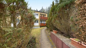 Un chemin menant à un bâtiment doté d’un balcon, entouré d’une végétation luxuriante.