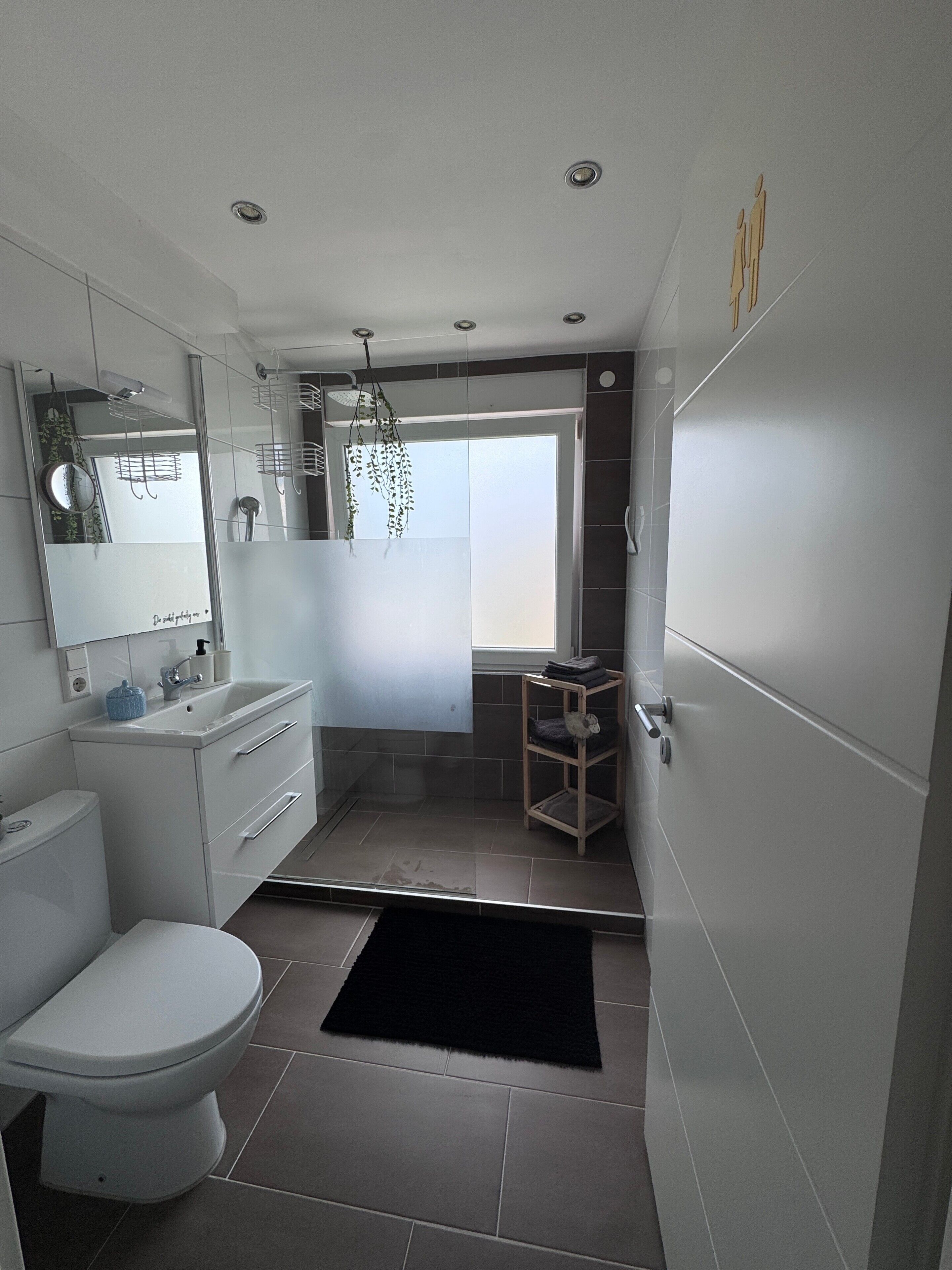 Ein modernes Badezimmer mit Toilette, Waschbecken, Spiegel und Fenster.