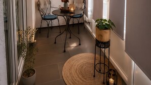 Un espacio interior acogedor con una mesa redonda, dos sillas, una planta colgante y una planta en maceta sobre un pedestal.