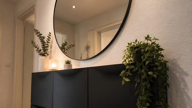 Un baño moderno con un espejo grande, muebles de color oscuro y una planta en maceta.