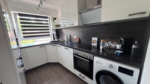 Una cocina moderna con armarios blancos, encimera negra, horno empotrado, microondas y lavadora.