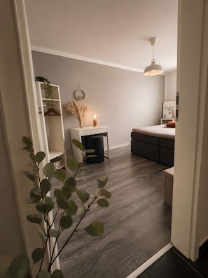 A modern living room with a wooden floor, a white sofa, a small side table with a lamp, and a wall-mounted light fixture.