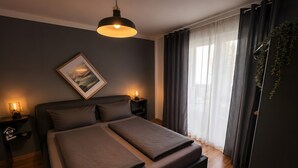 Un dormitorio moderno con cama, lámparas de noche, una lámpara colgante, un cuadro en la pared y una ventana con cortinas.