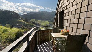Un balcon donnant sur une vallée, une table ornée d’un vase de fleurs et un mur en briques.