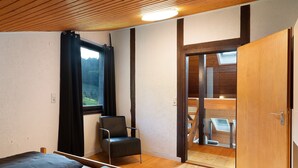 Une pièce comprenant un lit, une chaise, une fenêtre et une porte donnant sur une autre pièce.