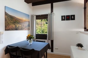 Un'area pranzo con tavolo, sedie, un vaso con fiori, un quadro e una finestra con tende.