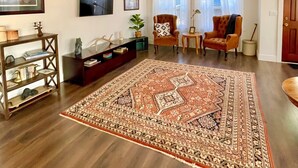 Ein geräumiges Wohnzimmer mit einem großen, gemusterten Teppich, einer Holz-Unterhaltungseinheit und zwei Sesseln.