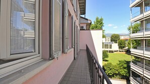 A balcony with a tiled floor, a metal railing, and a view of a building with multiple windows and a grassy area. - Amazing Lugano with private parking, close to the lake, Lugano, Switzerland (Lugano)
