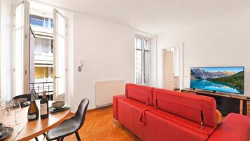 Uma sala de estar moderna com um sofá vermelho, uma mesa de jantar com cadeiras, uma televisão e vista para montanhas pela janela.
