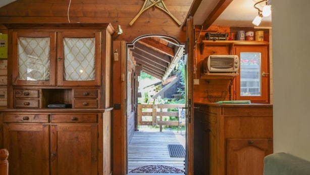 Un interior de madera con una zona de cocina, una escalera que lleva a una terraza exterior y una pequeña ventana con una decoración de estrella.