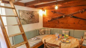 Una habitación acogedora con techo de madera, una mesa de madera con sillas, un banco y un cuadro en la pared.