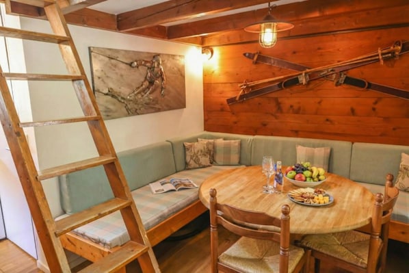 Una stanza accogliente con soffitto in legno, un tavolo in legno con sedie, una panca e un quadro appeso al muro.