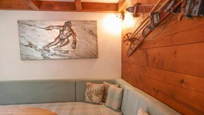 Una habitación acogedora con techo de madera, un sofá verde con cojines de cuadros, y un cuadro de un esquiador.
