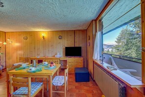 A wooden interior with a dining table, chairs, a television, and a window with a view of trees and mountains. - Appartamento Bareu Mountain View, Sauze d'Oulx, Italy (Sauze d'Oulx)