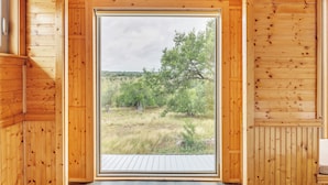 Una cabaña de madera con un ventanal amplio que ofrece vistas a un paisaje cubierto de hierba y árboles.