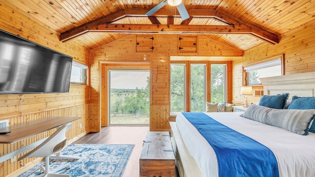 Un dormitorio de cabaña de madera con cama, escritorio, televisor y vistas al exterior.