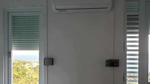 A bedroom with a bed, two windows with blinds, an air conditioning unit, and a door. - Wake Up to Ocean Views: Your Puerto Rico Paradise Awaits! (Yabucoa)