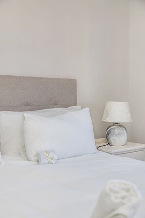 A hotel room with a bed, pillows, a bedside lamp, and a nightstand.