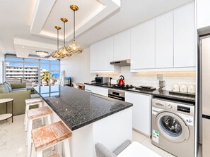 A modern kitchen with white cabinets, a granite countertop, a built-in washing machine, and a dining area with a view.