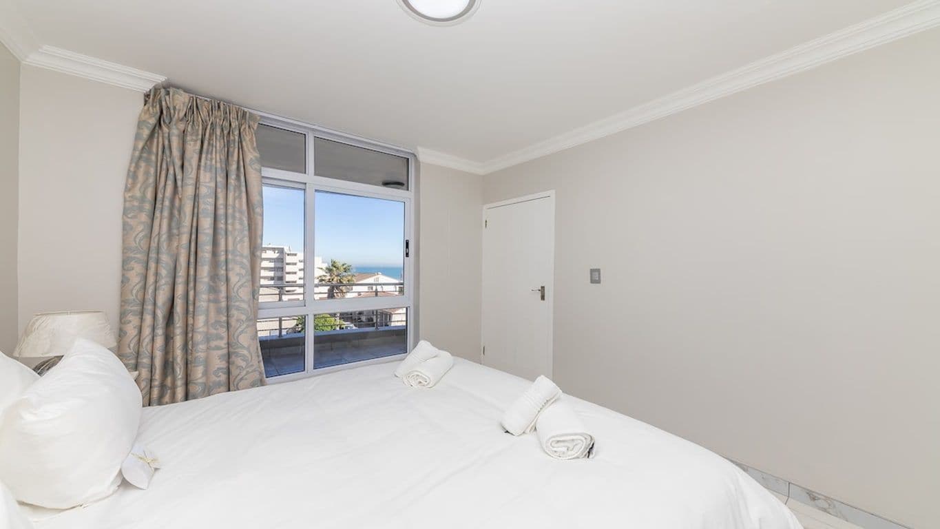 A hotel room with a large bed, a window with curtains, and a view of buildings outside.