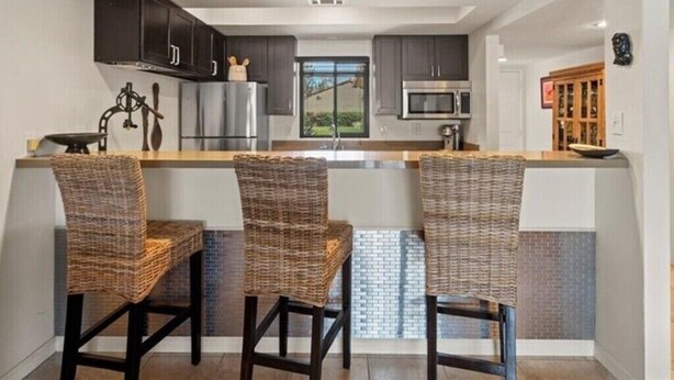 A modern kitchen with dark cabinets, a central island with bar stools, a microwave, and a large window. - Peaceful Waterfront Getaway (pet-friendly) (Palm Desert)