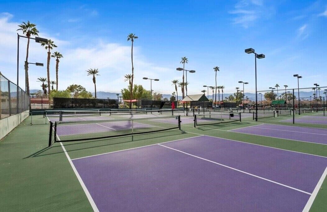 A tennis court with multiple courts, surrounded by palm trees and a clear sky.
